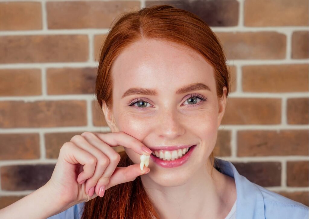 Young woman holding an extracted wisdom tooth, representing the final stage of wisdom tooth eruption and common treatment when a wisdom tooth does not come in properly.