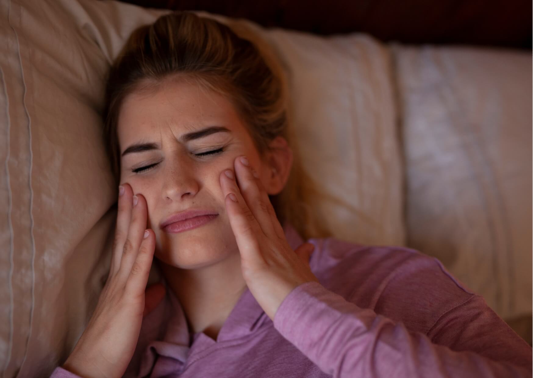 Woman experiencing jaw and facial discomfort from nighttime teeth grinding, highlighting common symptoms that may require treatment to fix grinded teeth and prevent further wear.
