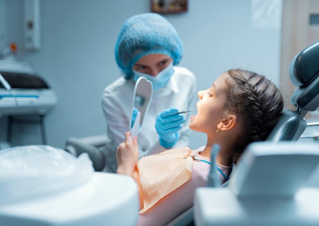 Pediatric dentist examining a child's teeth while checking the need for a dental spacer after early tooth loss.
