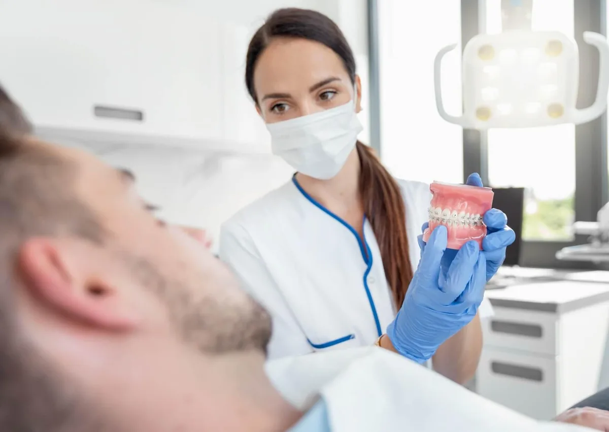 Dental professional showing a patient a braces model while discussing braces cost with insurance and treatment planning.